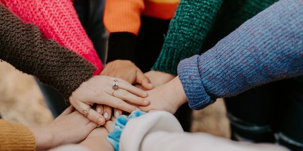 Eight hands sitting on top of each other signifying comradery and teamwork.