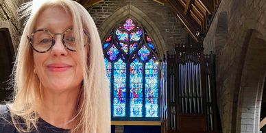 Woman smiling inside a church with stained glass windows.