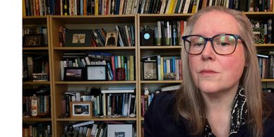 Woman with glasses sitting in front of a filled bookshelf.