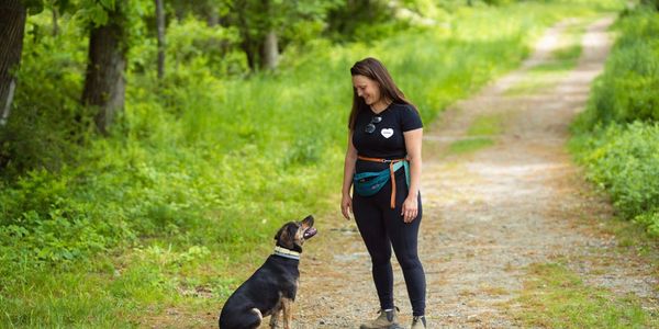 Woman training her dog in a green forest path.
