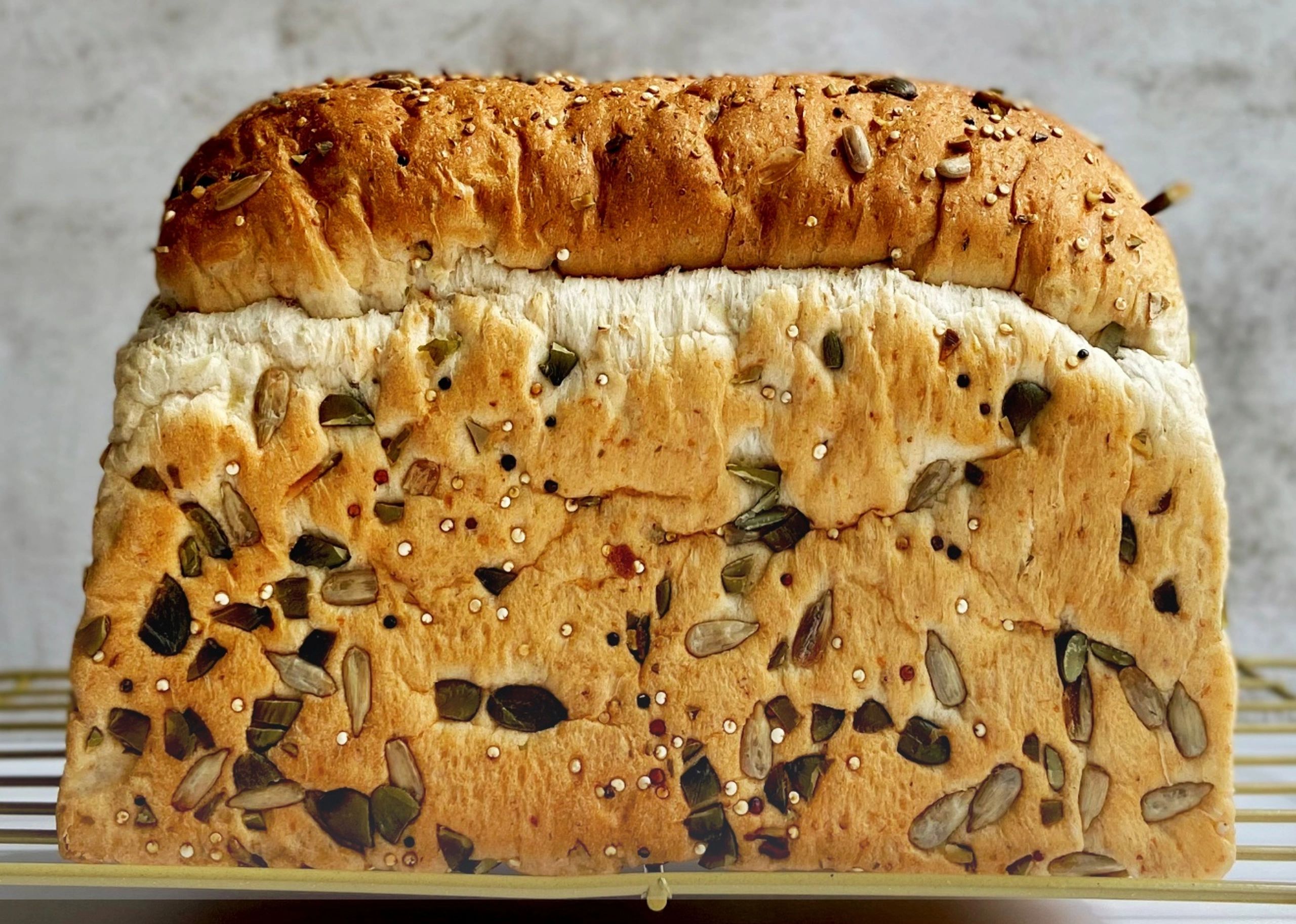 Freshly baked multigrain bread loaf with seeds cooling on a rack.