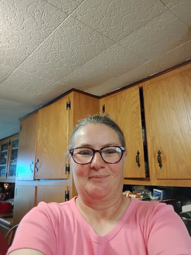 Smiling woman in glasses and pink shirt in a kitchen.