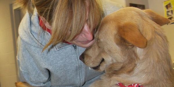 A woman affectionately holding a dog close indoors.