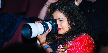 A woman with curly hair taking a photo using a professional camera.
