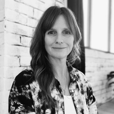 Black and white portrait of a smiling woman with long hair against a brick wall.