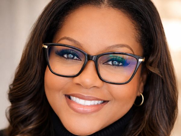 Smiling woman wearing glasses with wavy hair and hoop earrings.