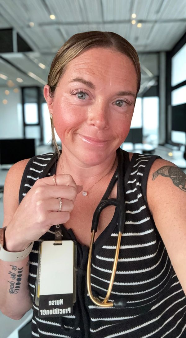 Smiling nurse practitioner with stethoscope and ID badge in a modern office.