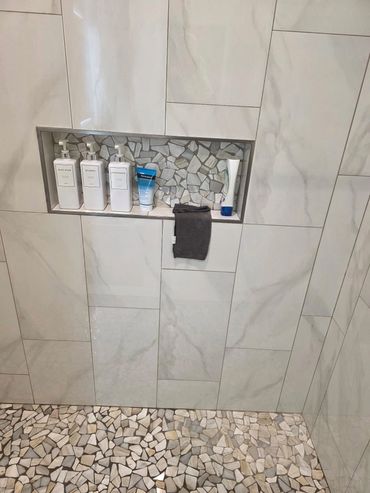 Walk-in tiled shower with built-in shampoo and soap niche in remodeled bathroom.