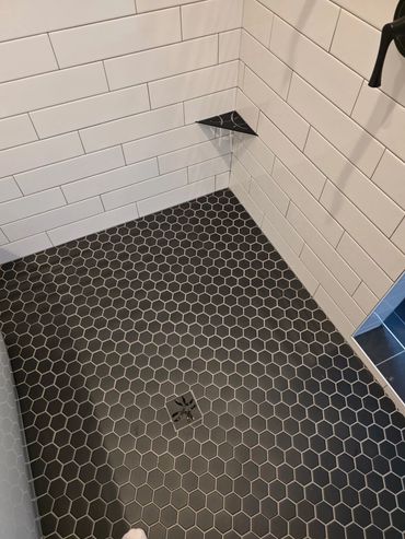 Walk-in shower with black tile and matching grout in remodeled bathroom.