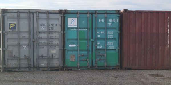 Three shipping containers lined up outdoors on a gravel surface.