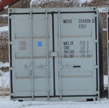 Gray shipping container with specifications printed on the door in snowy surroundings.
