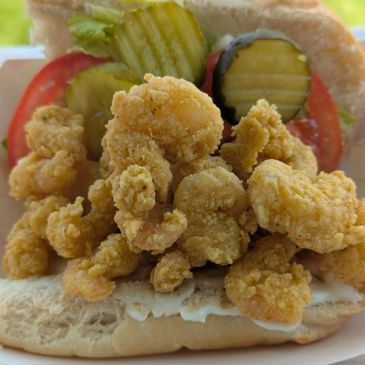 Close-up of a fried shrimp po' boy sandwich with pickles and tomatoes.