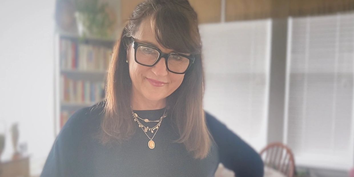 Woman wearing glasses and layered necklaces smiling indoors.