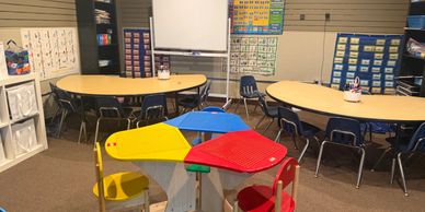 A colorful classroom with round tables and educational posters on the walls.
