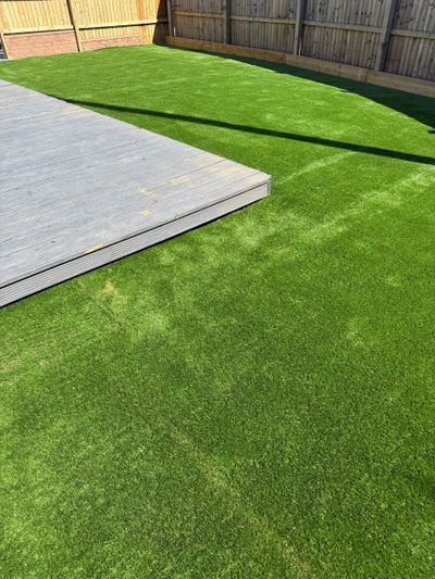 A backyard with fresh green synthetic grass and a wooden deck.