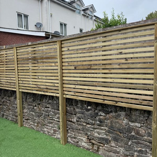 Wooden slatted fence over old stone wall with synthetic grass below.