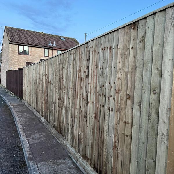 A tall wooden fence along a narrow sidewalk next to a house.
