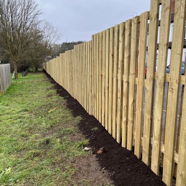 New wooden fence alongside a grassy path with fresh soil.
