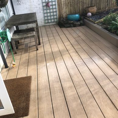 A tidy wooden patio deck with garden furniture and plants.
