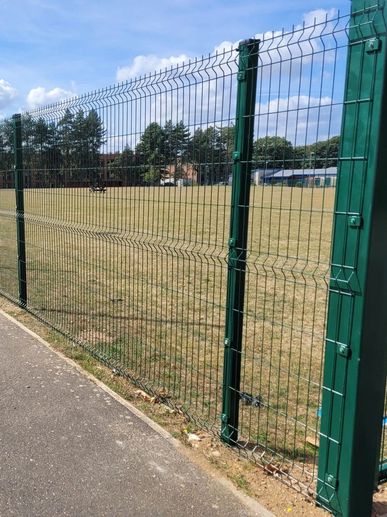 Green metal fence enclosing a grassy field under a sunny sky.