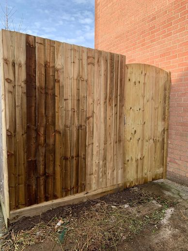 Partially stained wooden fence and gate against a brick wall.