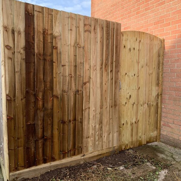 New wooden fence and gate next to a brick wall under blue sky.