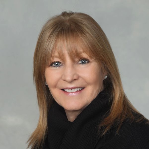 Smiling woman with light brown hair and blue eyes wearing a black sweater.