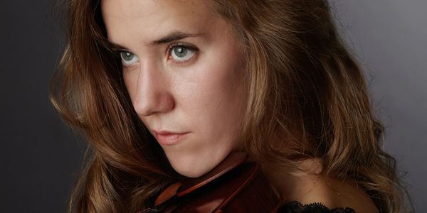 Close-up of a woman with intense green eyes holding a violin.