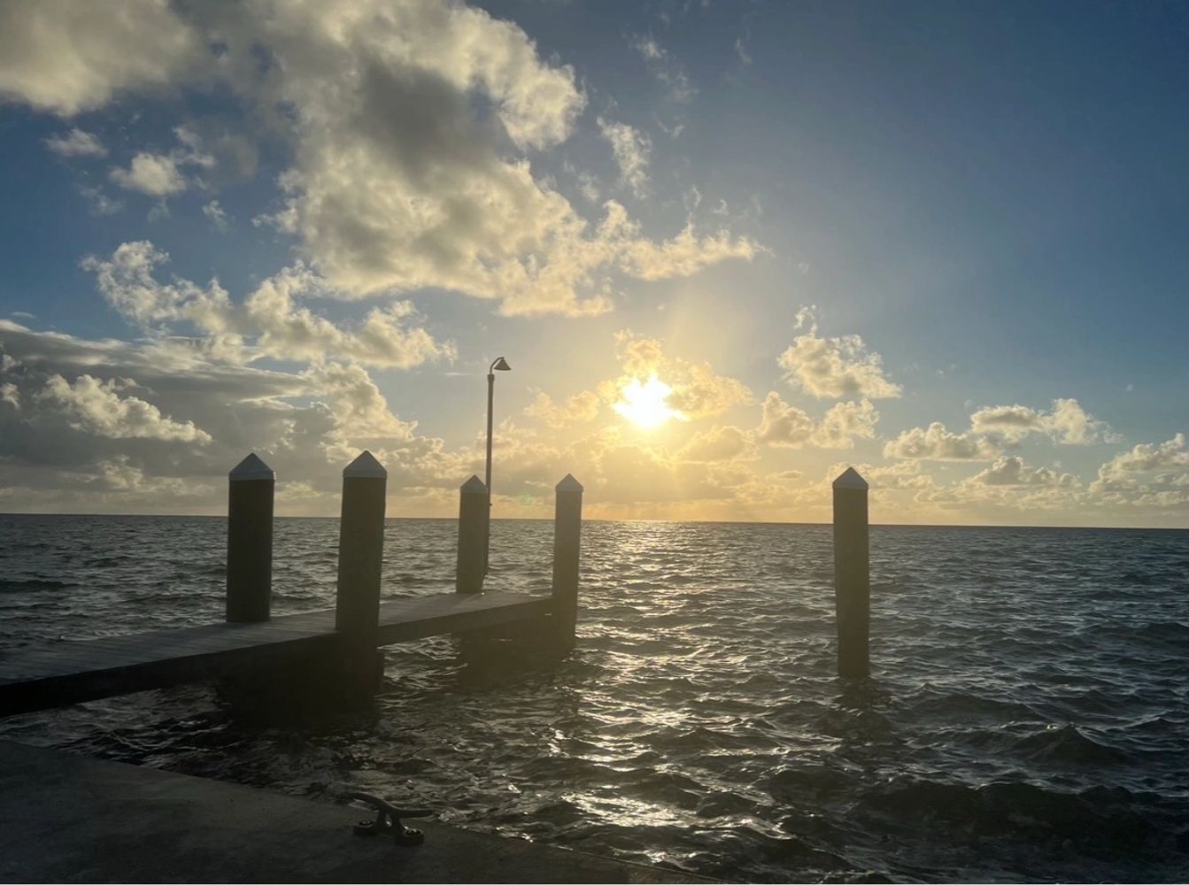 Sunset over a pier with calm sea and scattered clouds.