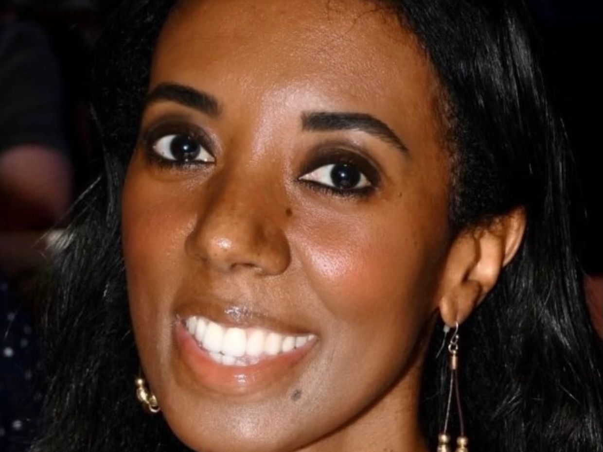 Woman smiling in a floral dress with dangling earrings.