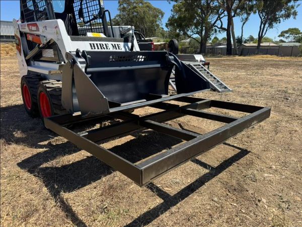 A skid steer loader with a metal attachment frame in a dry outdoor area.