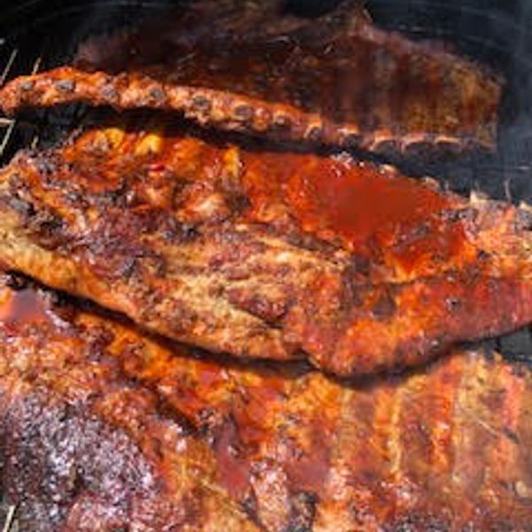 Grilled BBQ ribs coated with sauce on a smoker grill.
