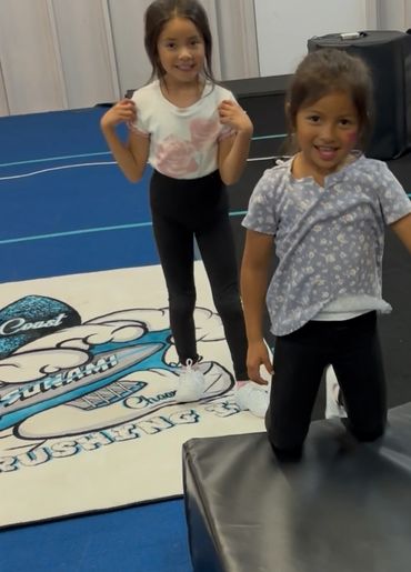 Two young girls smiling and posing in a cheerleading gym.