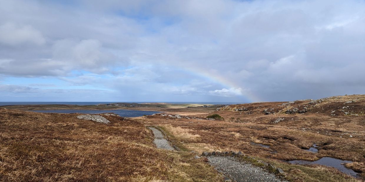 A faint rainbow over a rugged moorland with a gravel path.