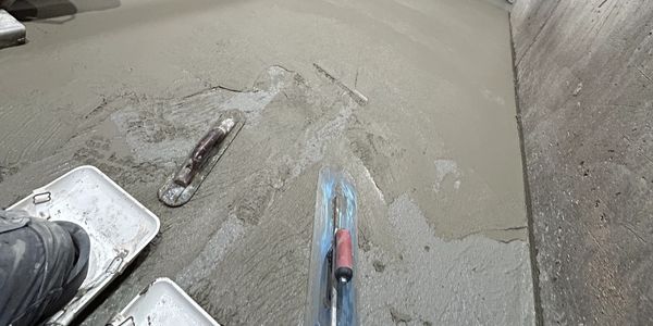 Fresh concrete being smoothed in an industrial basement with machinery around.