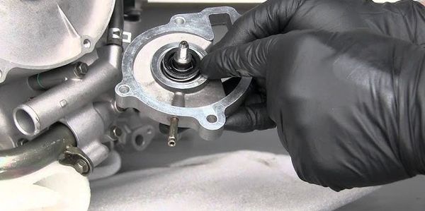 Hand in black glove working on a mechanical part of an engine.