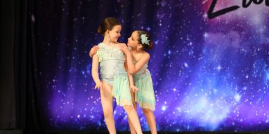Two young girls in matching dance costumes on stage.