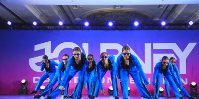 Group of dancers in blue outfits performing on stage.