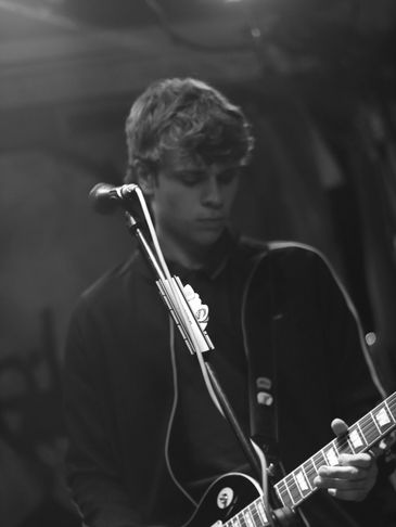 A young man playing guitar on stage in black and white.