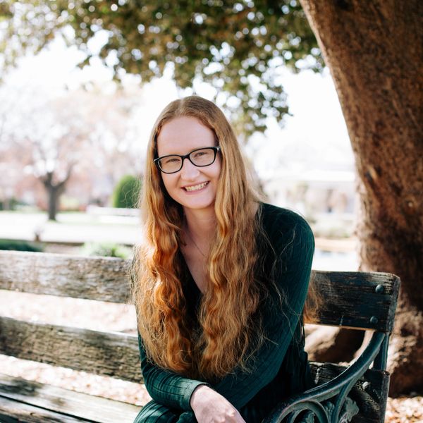Smiling woman with long hair sitting on a bench outdoors.