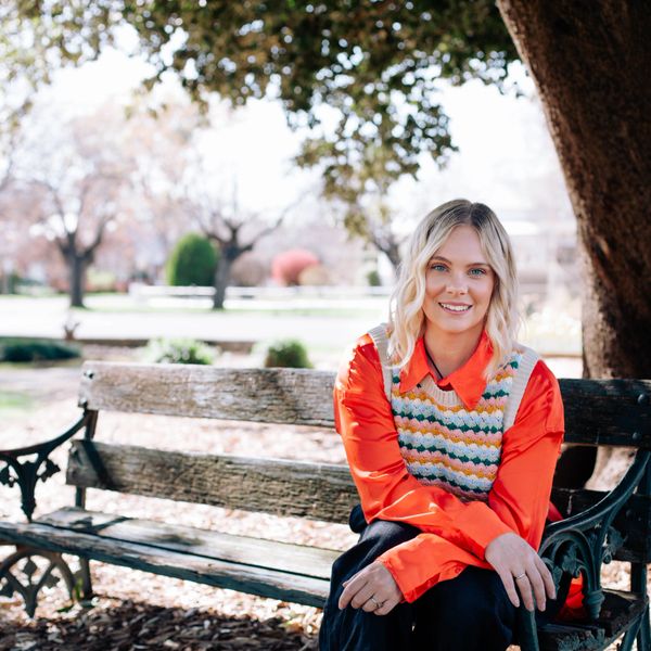 Woman with blonde hair sitting on a park bench under a tree.