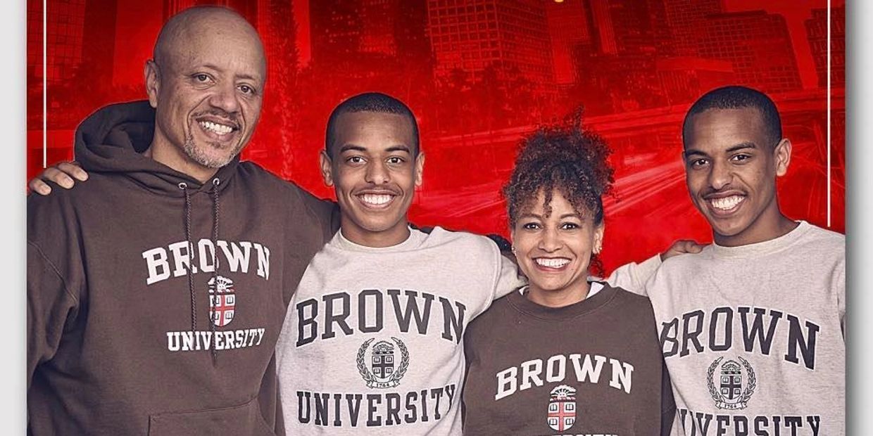 A smiling family wearing Brown University sweatshirts against a red city backdrop.