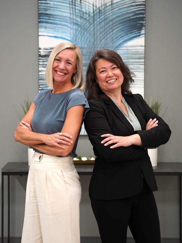 Two confident women standing back-to-back with arms crossed, smiling.