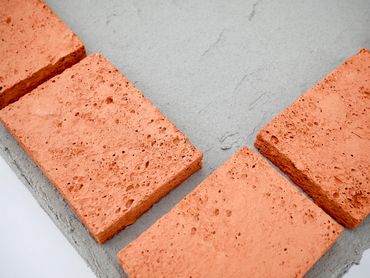 Close-up of red bricks arranged on a gray concrete surface.