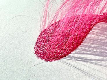 Close-up of pink threads arranged in a curved, textured shape casting shadows.