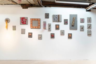 Art installation with concrete and brick pieces arranged on a white wall.