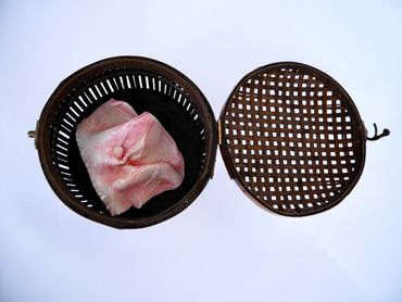A wooden basket with a raw pork piece inside.