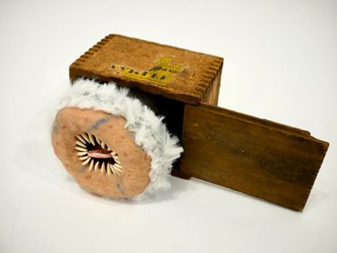 A wooden box with a sliding door and a plush, furry circular object inside.