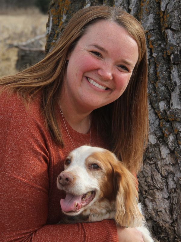 Woman smiling while hugging a happy dog outdoors.