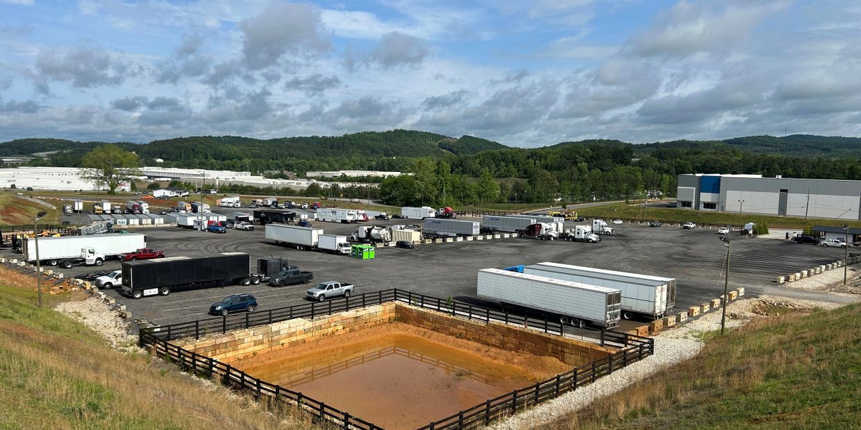 A large truck parking lot with multiple trailers and vehicles under a cloudy sky.
